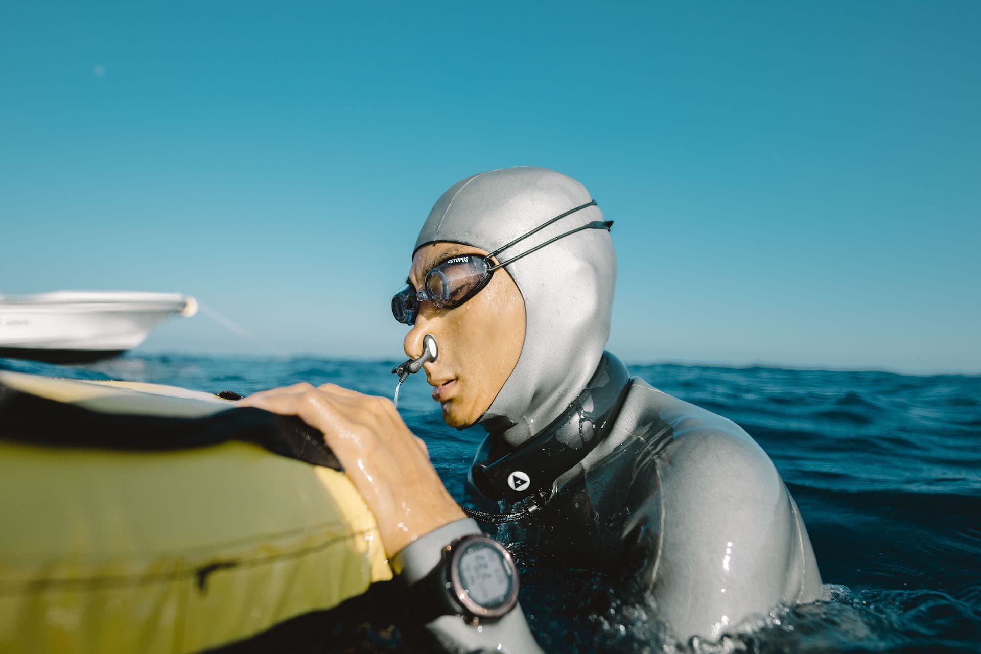 man in wetsuit at sea holding on to buoy