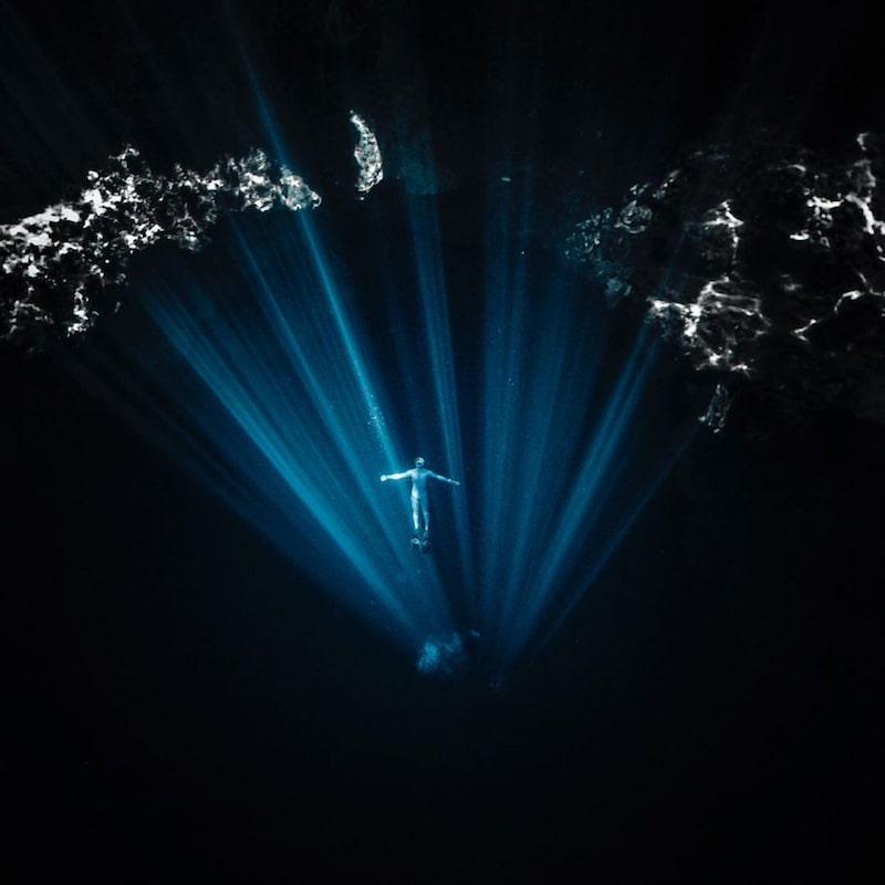 freediver in a dark cenote wearing a blue suit and alchemy v330 pro carbon fins