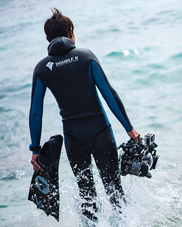 man holding a camera and alchemy v3 pro carbon fins entering the sea